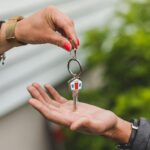Close-up of a hand handing over a key with a house keychain, symbolizing real estate transaction.